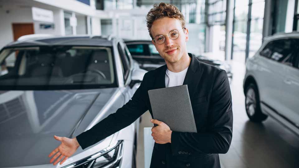 Ein Verkäufer zeigt auf ein Auto und erklärt dem Kunden die Konditionen beim Auto verkaufen Dachau